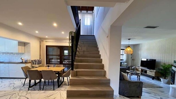 Un intérieur moderne avec un escalier menant à un niveau supérieur, un coin repas doté d’un sol en marbre et un espace de vie avec un téléviseur et des sièges.