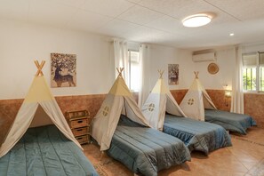 A room with four beds, each with a teepee-style canopy, a large window, and a wall-mounted air conditioner.