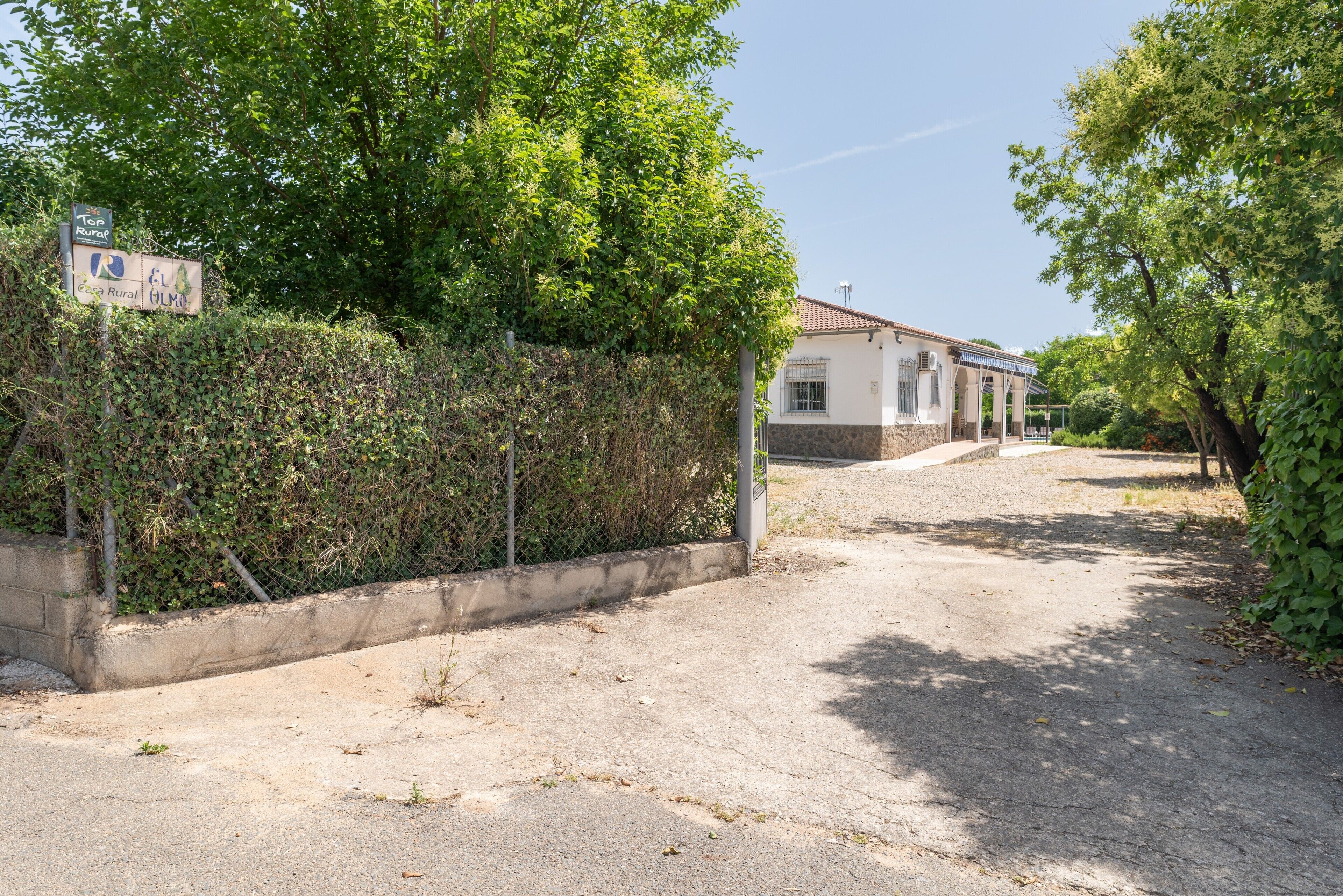 Une propriété rurale avec une allée pavée, un bâtiment blanc doté d’un toit en tuiles et une enseigne indiquant « Top Rural El Almor ».