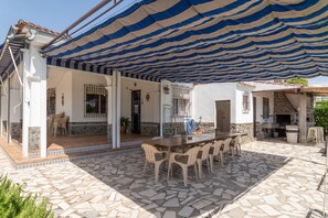 Un patio exterior con un toldo a rayas, suelo de baldosas de piedra y una mesa de madera con sillas.