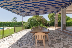 An outdoor patio with a striped awning, a stone-tiled floor, a wooden table, and chairs. - Country House 'El Olmo - Families Only' with Mountain Views, Wi-Fi and Air Conditioning (Palma del Río)