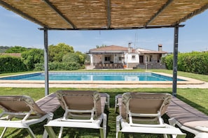 A covered outdoor seating area with lounge chairs facing a swimming pool and a house in the background. - Country House 'El Olmo - Families Only' with Mountain Views, Wi-Fi and Air Conditioning (Palma del Río)