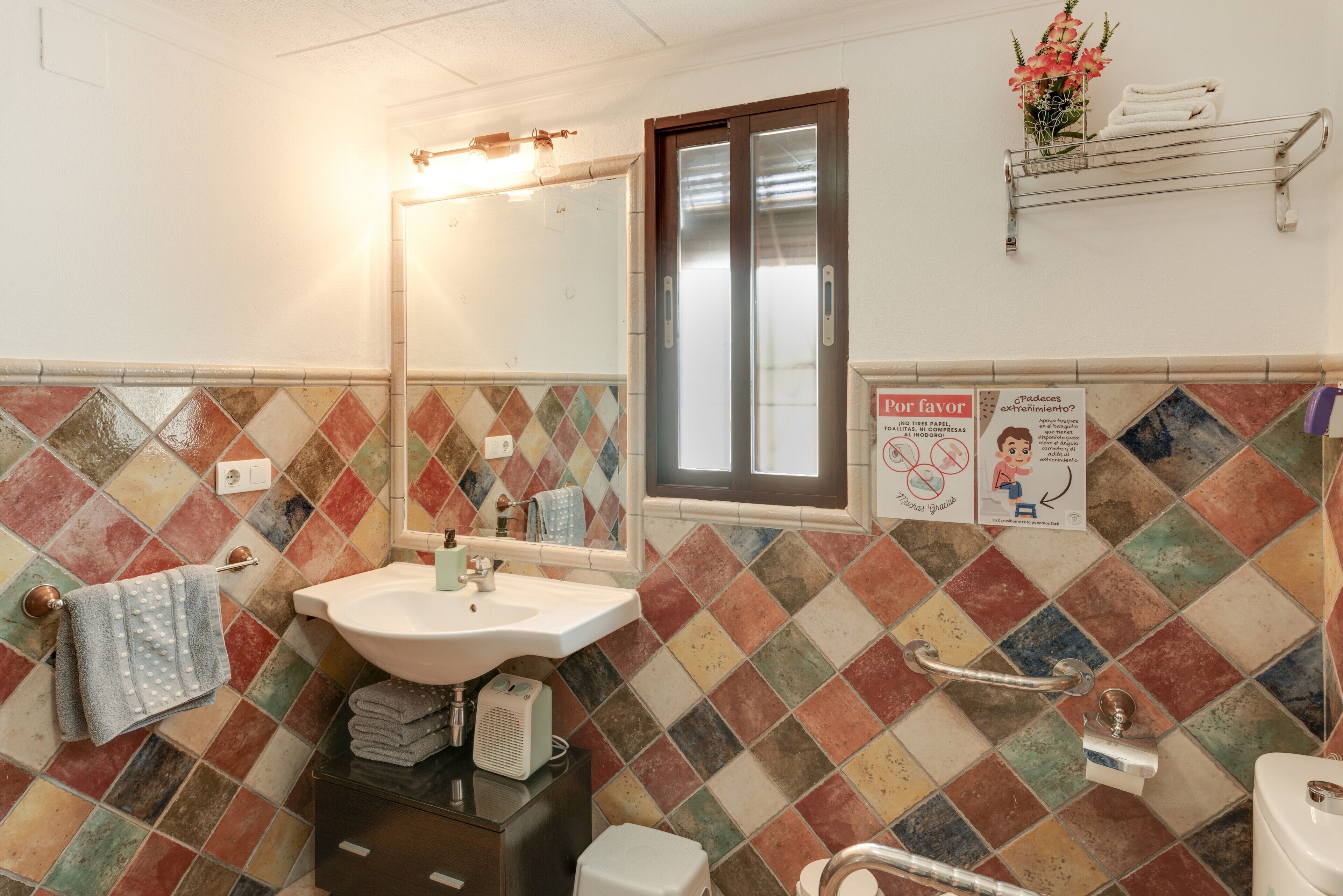 Ein Badezimmer mit Waschbecken, Spiegel, Fenster und farbenfrohen Fliesen.