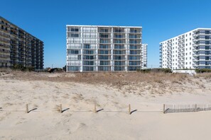 A modern multi-story building with a grid-like facade, located adjacent to a sandy beach area with a wooden fence in the foreground. - Oceanfront Escape on 132nd Street (Ocean City)