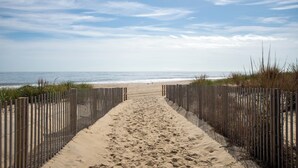 A sandy beach path leading to the ocean, flanked by wooden fences.