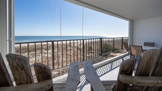 A balcony with wooden chairs and a view of the beach.