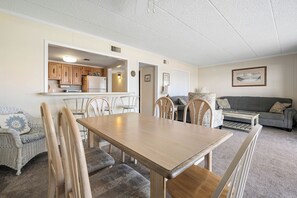 A dining area with a wooden table and chairs, a kitchen in the background, a grey sofa, and a framed picture on the wall. - Oceanfront Escape on 132nd Street (Ocean City)