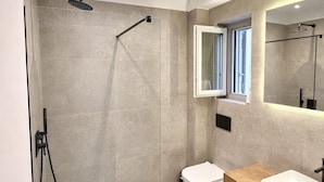 A modern bathroom with a glass-enclosed shower, a wooden vanity, and a large mirror. - Villa Lithos Sea View (Paros)