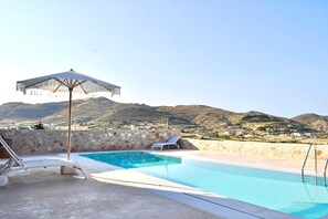 A swimming pool with a clear view of the surrounding landscape, a stone wall, and a lounge chair. - Villa Lithos Sea View (Paros)