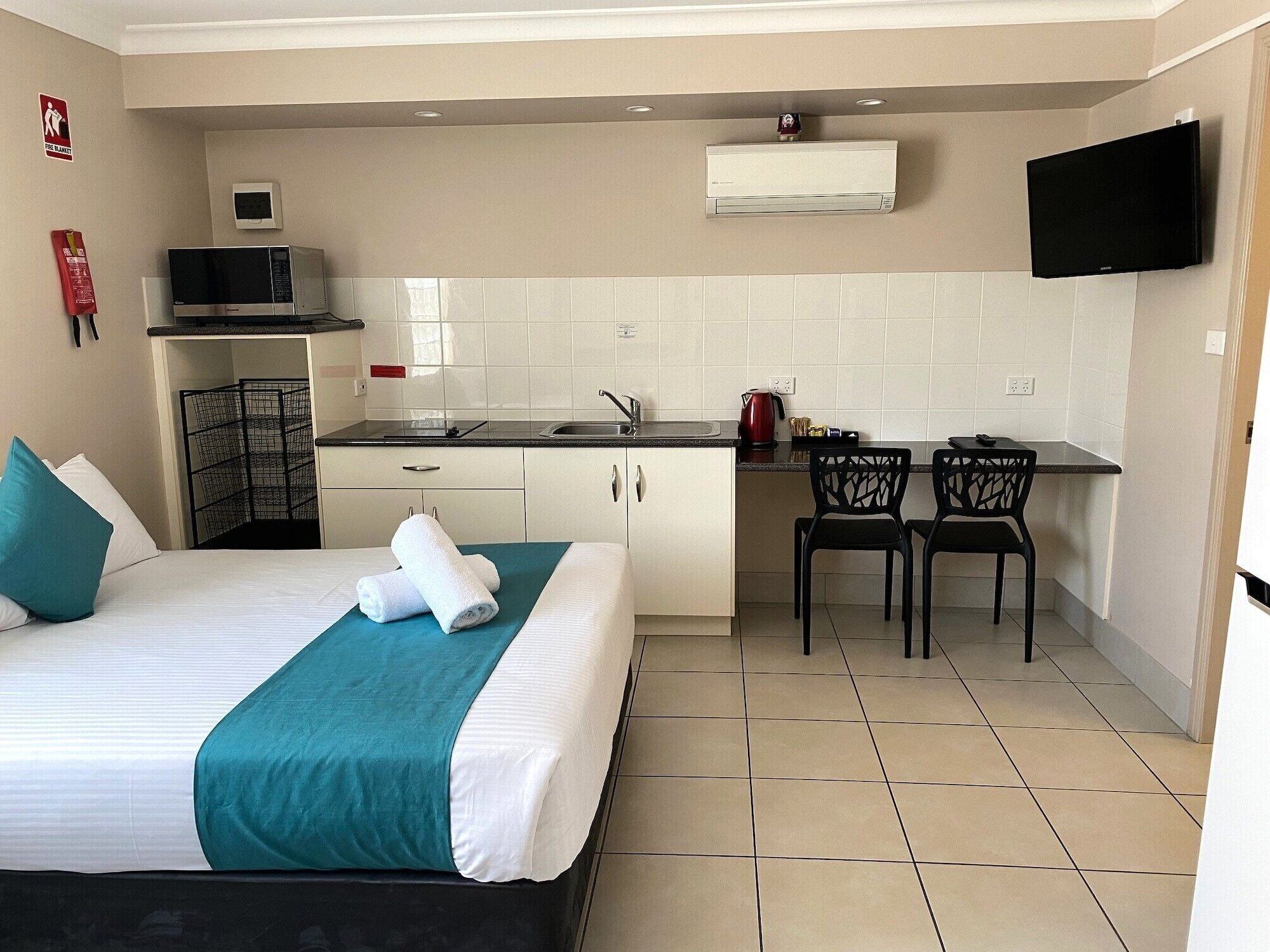 Una habitación de hotel compacta con cama, kitchenette, televisor y un pequeño comedor.