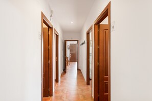 A hallway with wooden doors and tiled flooring, leading to a room with a bed and a window. - Country House 'La Sierrezuela - Families Only' with Mountain Views, Wi-Fi & Air Conditioning (Posadas)