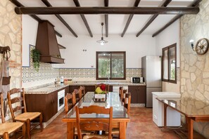 A kitchen with a dining table, chairs, a refrigerator, and a stone wall. - Country House 'La Sierrezuela - Families Only' with Mountain Views, Wi-Fi & Air Conditioning (Posadas)