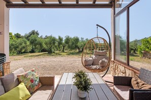 A covered outdoor seating area with a hanging chair, a table with a potted plant, and a view of a vineyard. - Country House 'La Sierrezuela - Families Only' with Mountain Views, Wi-Fi & Air Conditioning (Posadas)