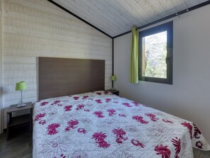 A bedroom with a wooden headboard, a bed with a floral bedspread, a nightstand with a lamp, and a window with a curtain.