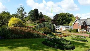 A well-maintained garden with manicured lawns and flower beds, a flagpole, and a traditional building with a pitched roof. - Morpeth Lodge (Morpeth)