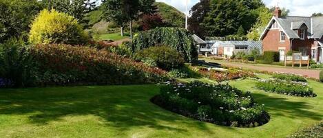 A well-maintained garden with manicured lawns and flower beds, a flagpole, and a traditional building with a pitched roof.