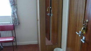 A room with a red chair, a wooden wardrobe, a door, and a small trash bin. - Morpeth Lodge (Morpeth)