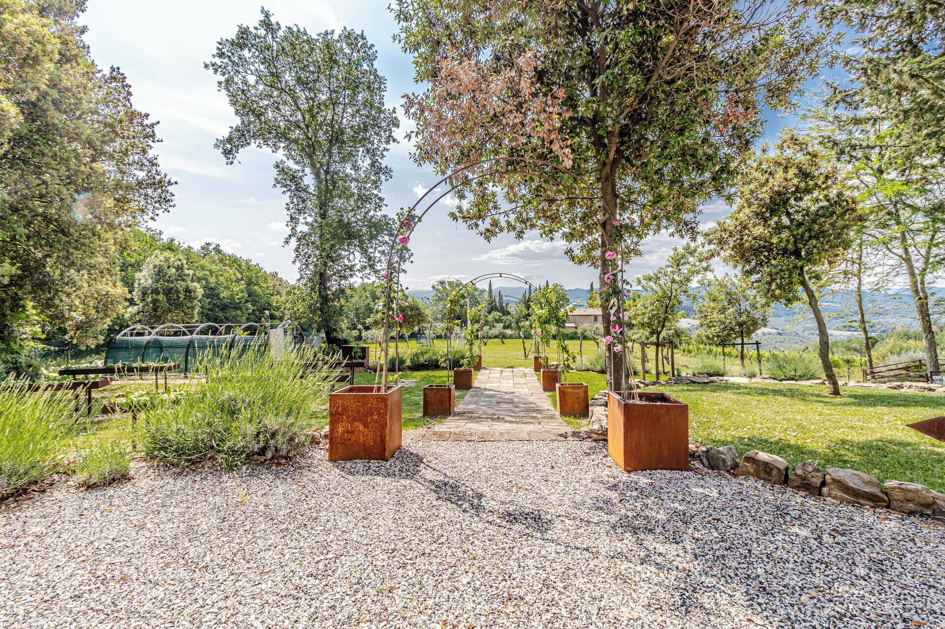 A gravel pathway leading through a garden with trees and planters.