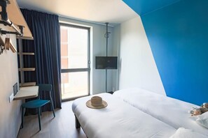 A hotel room with a bed, a desk, a chair, a TV, and a large window. - Ibis Budget La Rochelle Centre (La Rochelle)