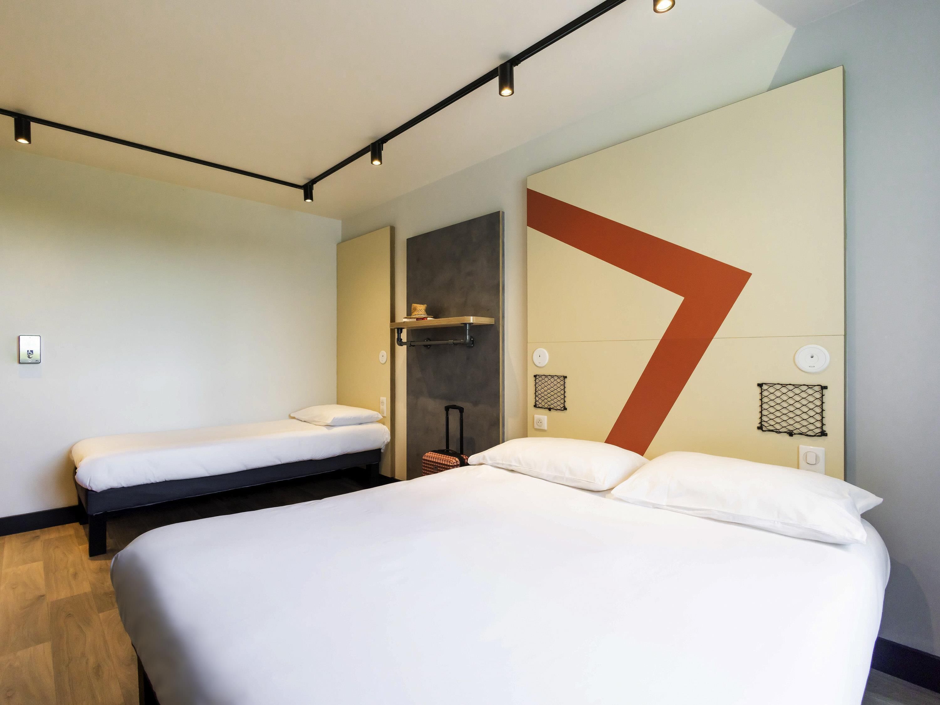 Habitación de hotel con una cama grande, una cama más pequeña, un escritorio y una silla.
