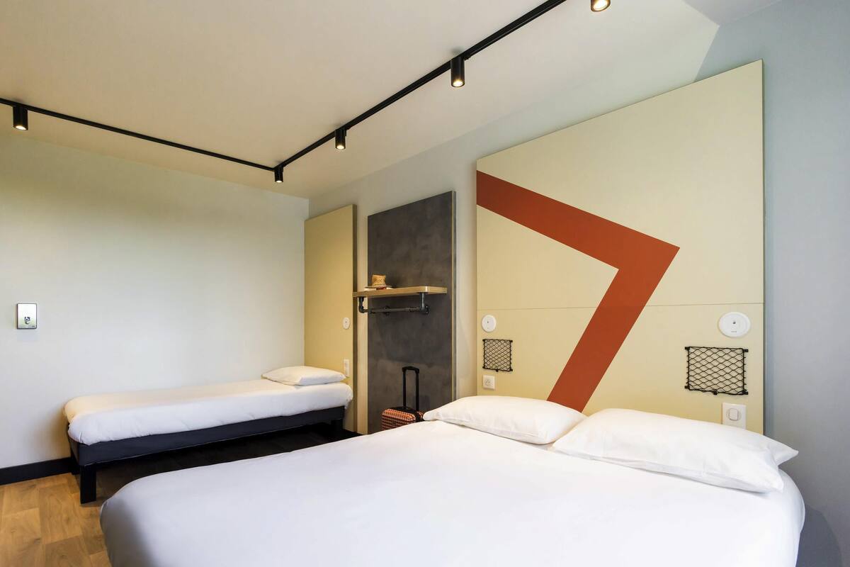 Ein Hotelzimmer mit einem großen Bett, einem kleineren Bett, einem Schreibtisch und einem Sessel.