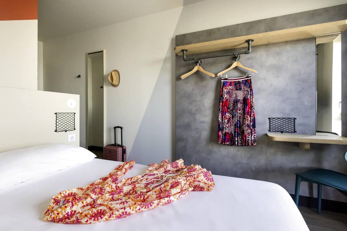 Ein Hotelzimmer mit Bett, Koffer, Kleiderständer und Spiegel.