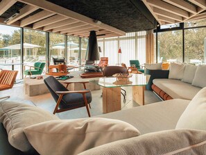 A spacious living area with a glass table, comfortable seating, and a large window offering a view of the outdoors.