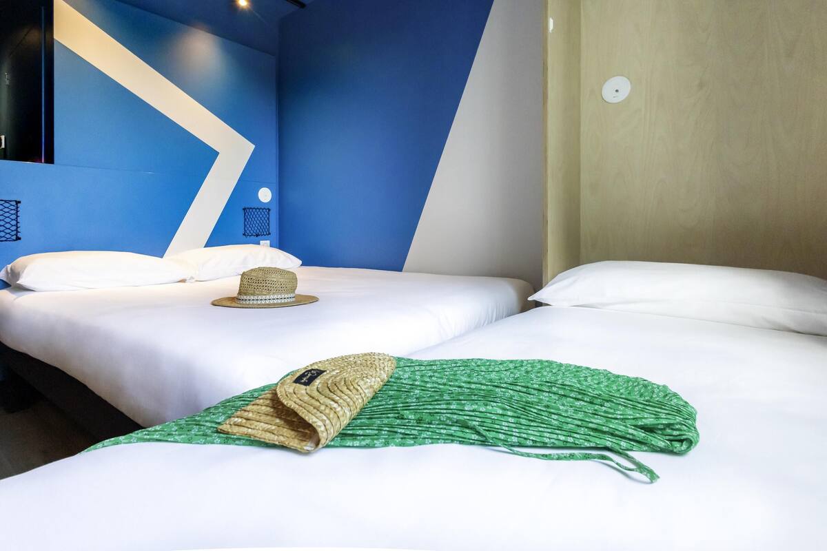 Ein Hotelzimmer mit zwei Betten, einem Hut und einem grünen Handtuch auf dem Boden.