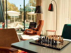 A chessboard on a table in a room with a view of outdoor seating and umbrellas. - Ibis Budget La Rochelle Centre (La Rochelle)