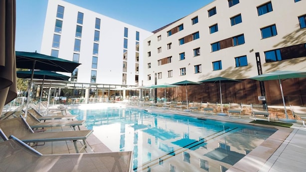 A swimming pool with lounge chairs, umbrellas, and a modern building in the background.