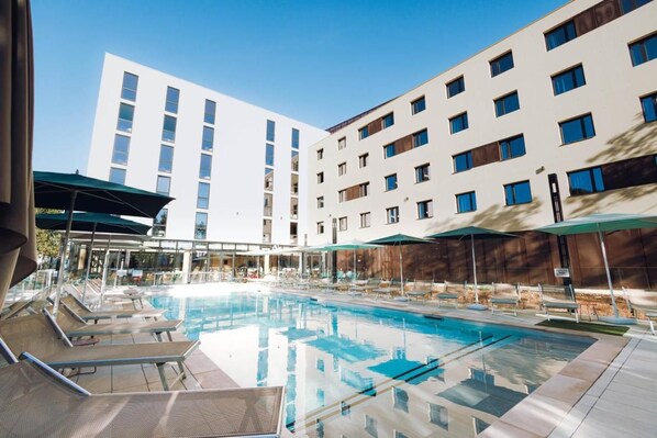 A swimming pool with lounge chairs, umbrellas, and a modern building in the background.