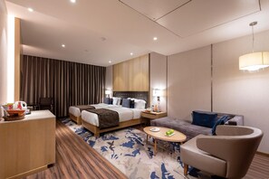 A hotel room with a bed, a sofa, a chair, a small table, and a desk. - Regenta Central Rajkot (Rajkot)