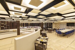 A modern hotel lobby with a curved reception desk, multiple dining tables, and a large flat-screen TV on the wall. - Regenta Central Rajkot (Rajkot)