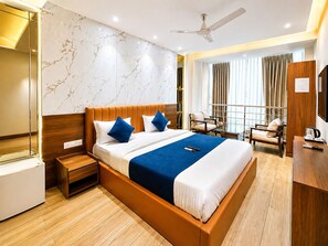 Une chambre d’hôtel avec un grand lit, un bureau, une chaise, un ventilateur de plafond et une vue sur l’extérieur.