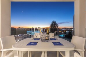 A balcony table with a view of a cityscape at dusk, a bottle of champagne, and ice in a bucket. - Correeira Luxury Residence F (Albufeira)