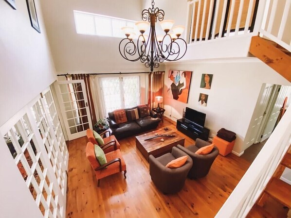 Uma sala de estar ampla com piso de madeira, um sofá de couro preto, uma mesa de centro de madeira e um candelabro.