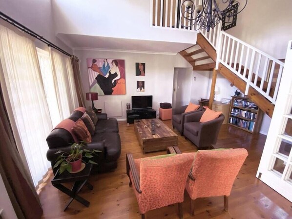 Een woonkamer met een bank, fauteuils, een salontafel, een televisie en een boekenkast.