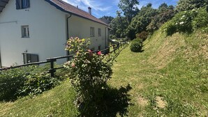Ein weißes Gebäude mit roten Ziegeln, einem Holzzaun und einem grasbewachsenen Hügel mit Bäumen.
