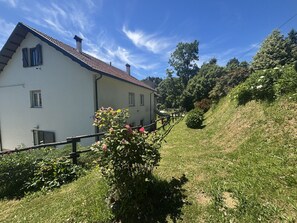 Ein weißes Gebäude mit roten Ziegeln, einem Holzzaun und einem grasbewachsenen Hügel mit Bäumen.