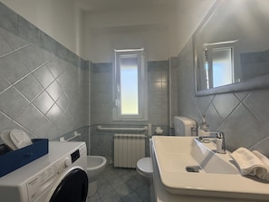 Ein kleines Badezimmer mit Waschmaschine, Toilette, Heizkörper und einem Waschbecken mit Handtuch.