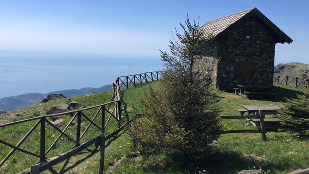 Eine Steinhütte mit Picknicktisch und Holzzaun mit Blick auf eine gebirgige Landschaft.