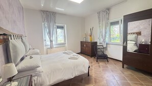 Ein Schlafzimmer mit einem Bett, einem Schreibtisch, einem Stuhl, einer Kommode und zwei Fenstern mit Vorhängen.