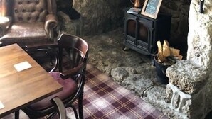 Ein rustikaler Raum mit Kamin aus Stein, einem Holztisch und einem bequemen Sessel.