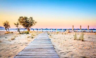 Un camino de madera que lleva a una playa con sombrillas y sillas.
