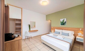 Una habitación de hotel moderna con una cama grande, un cabecero de madera, un escritorio pequeño con una cafetera, una silla blanca y un espejo.