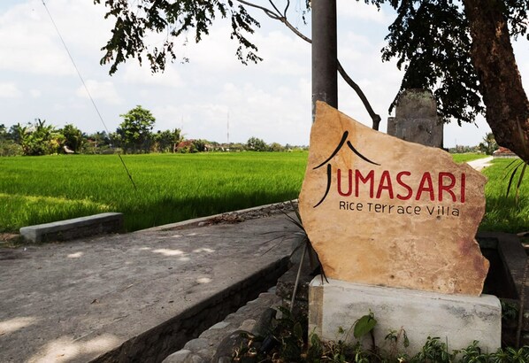 A sign for Jumasari Rice Terrace Villas with a view of a green rice field in the background. - Uma Sari Rice Terrace (Mengwi)