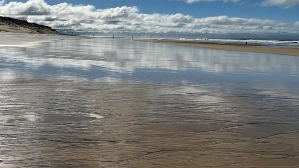 Una playa con cielo despejado y agua tranquila que refleja las nubes.