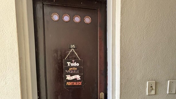 A dark brown door with a sign that reads "Tudo pode naquele fortece" and a number "35" above it. - Cozy Studio Apartment Praia Grande Ocian (Praia Grande)