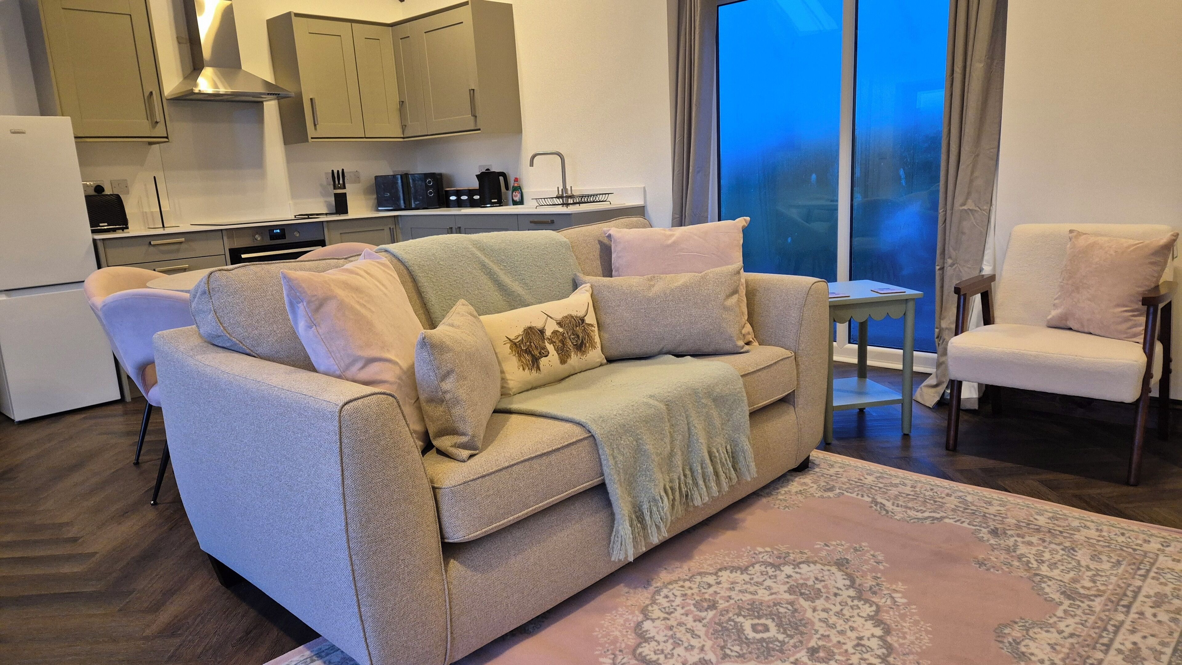 A modern living room with a sofa, a chair, a coffee table, and a kitchen in the background.