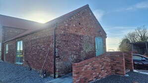 Un bâtiment en briques avec une porte et des fenêtres, une allée gravillonnée et une voiture garée à proximité.